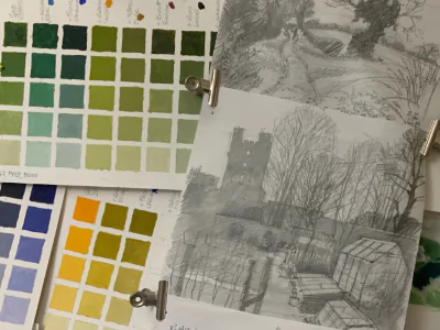 A pin board with a pencil sketch of a landscape and sheets testing green colour mixes in several grids